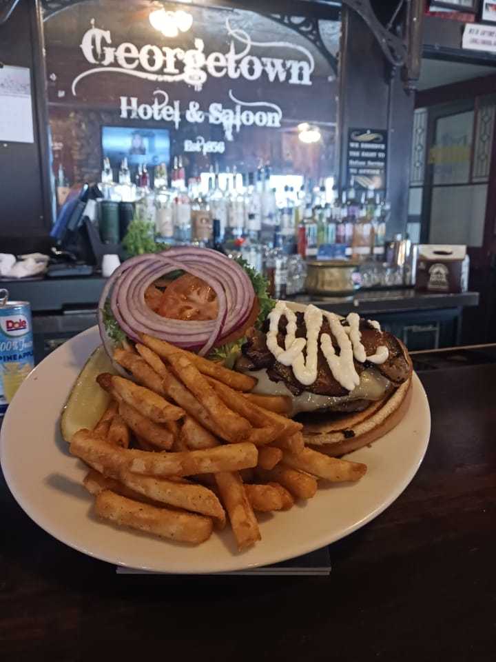 Burger with fries, onion, lettuce, and pickle served at Georgetown Hotel & Saloon bar.