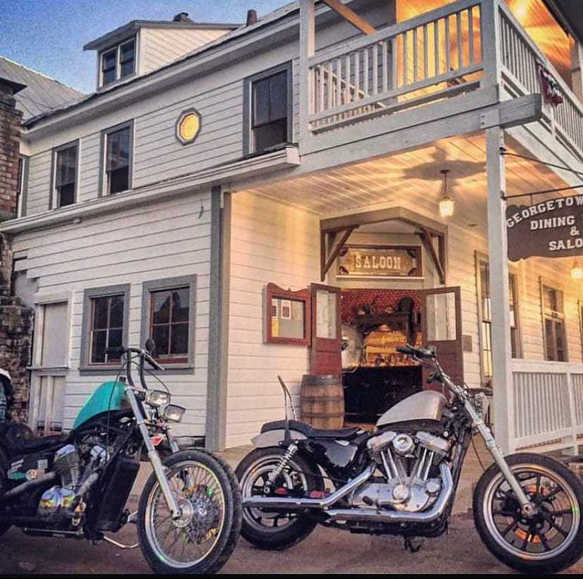 Two motorcycles parked outside an old-style saloon at dusk.