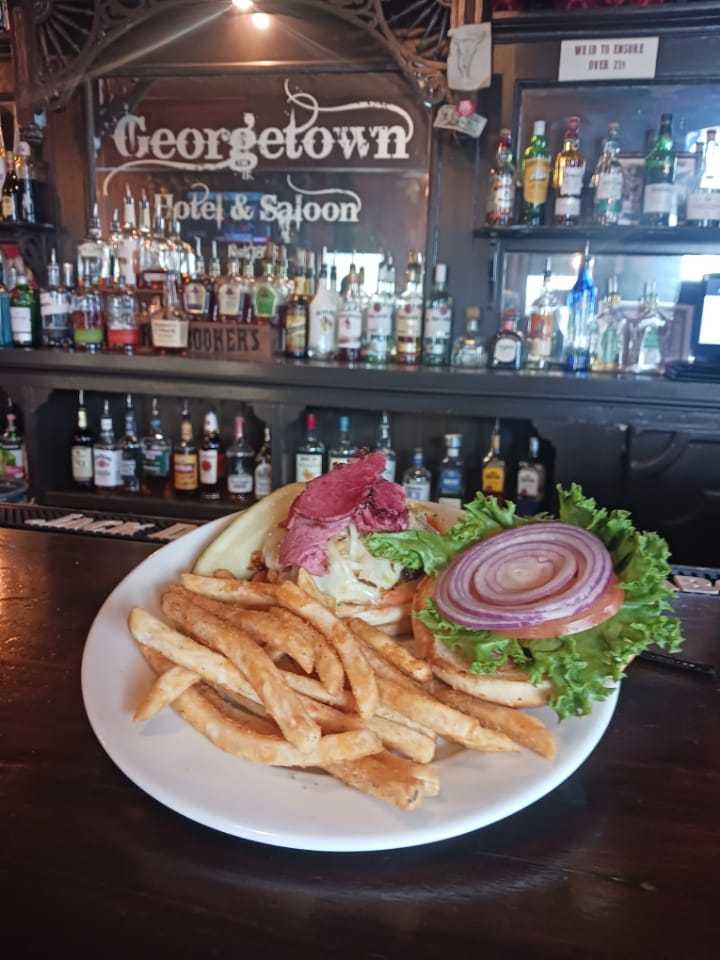Plate of fries and a sandwich with lettuce, tomato, and onion in a bar setting.
